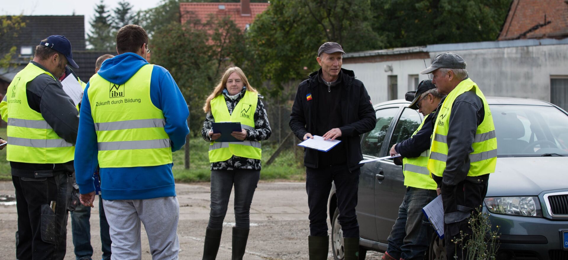 Menschen stehen in Warnwesten im Kreis und bespreche sich auf einem Hof